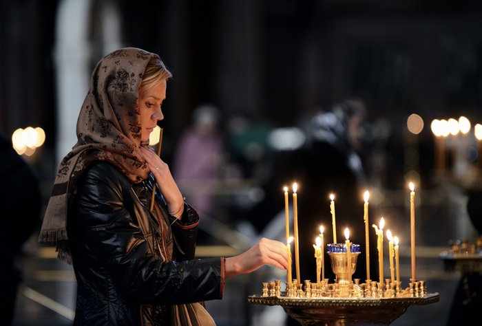 Женщина ставит свечку в церкви